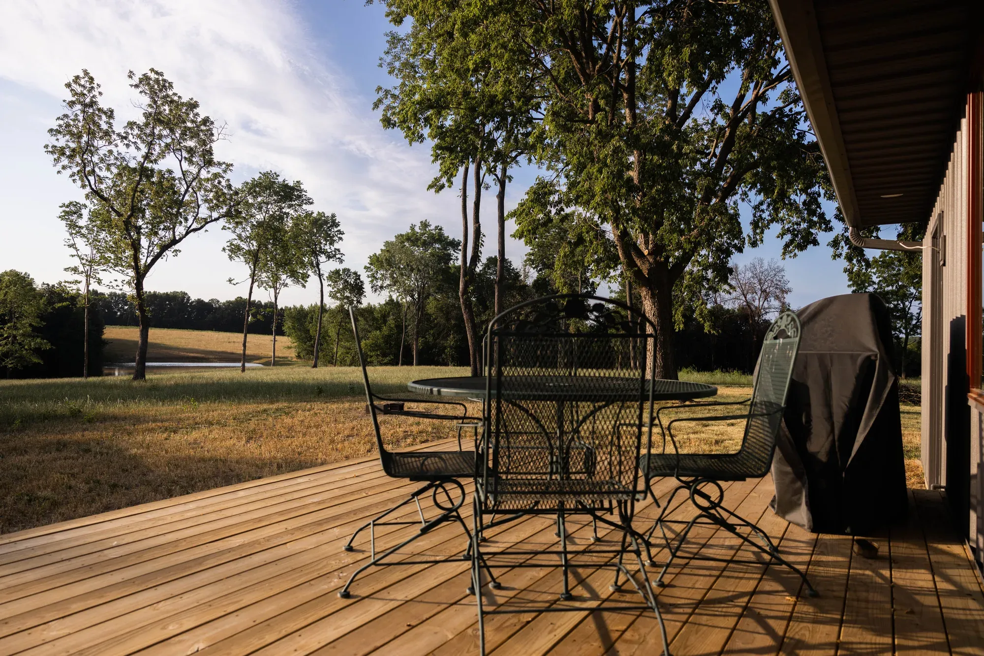 Deck with a table, chairs and a covered grill, looking out over open fields