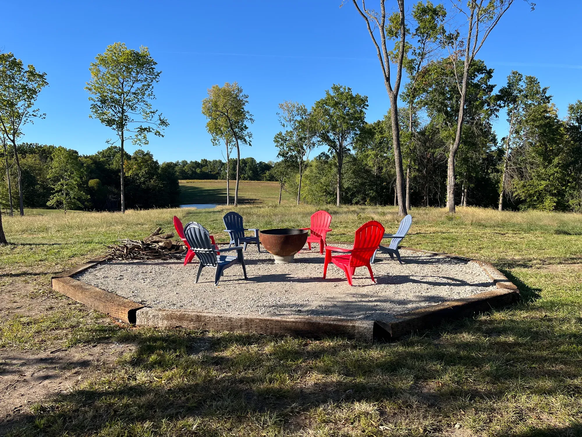 Fire pit with red and blue Adirondack chairs on a gravel circle