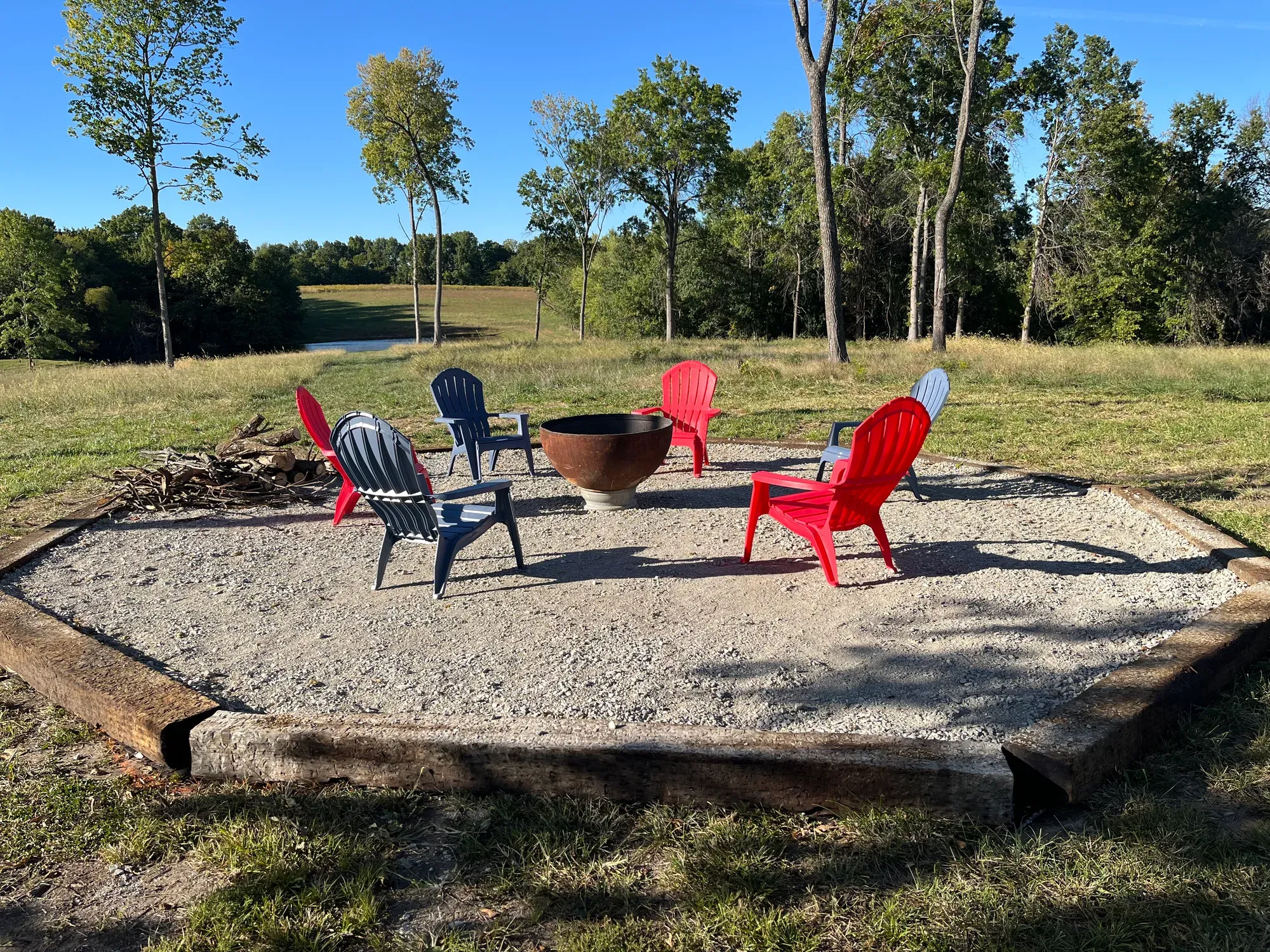 Gravel fire pit circle with Adirondack chairs and a stack of firewood