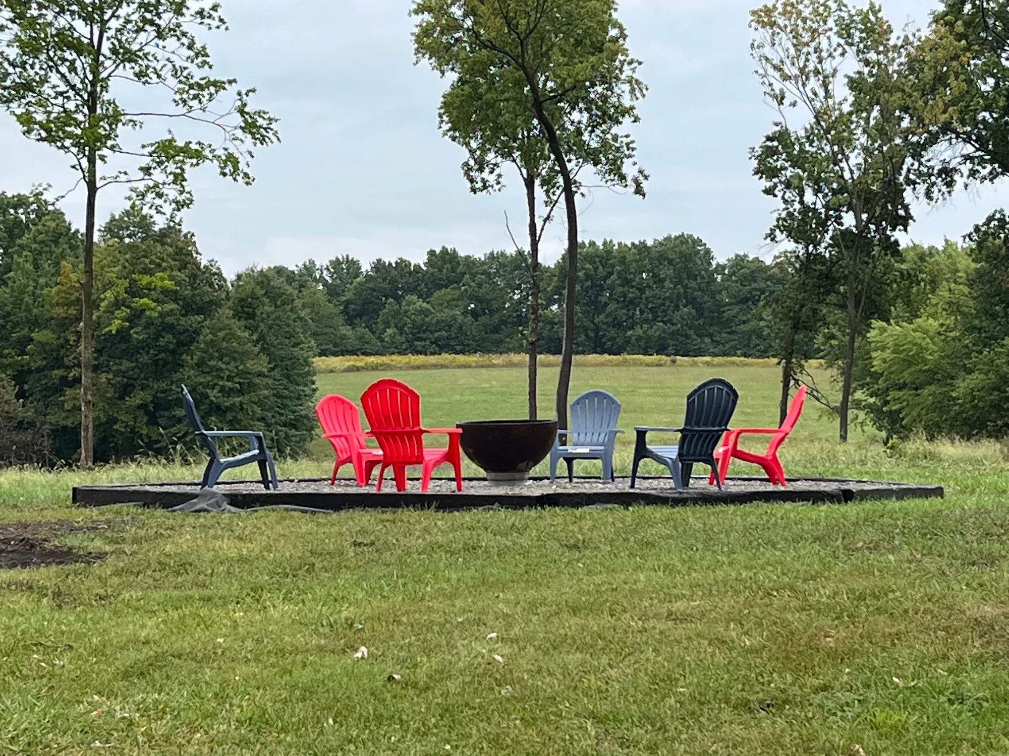Adirondack chairs around the fire pit with a field and trees beyond